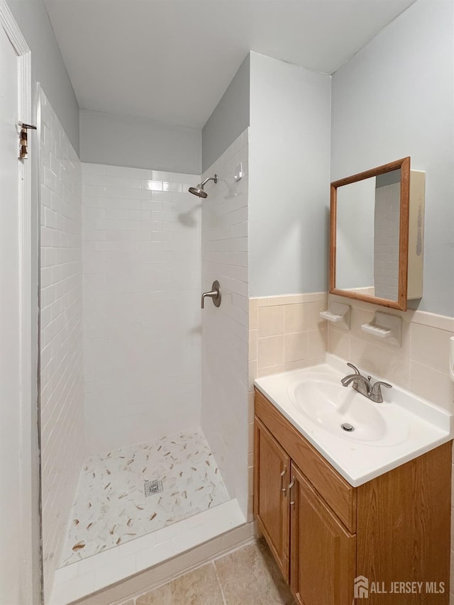 bathroom with tile walls, tile patterned flooring, a shower stall, and vanity