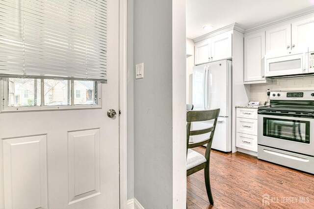 kitchen featuring white appliances, hardwood / wood-style floors, tasteful backsplash, and white cabinetry