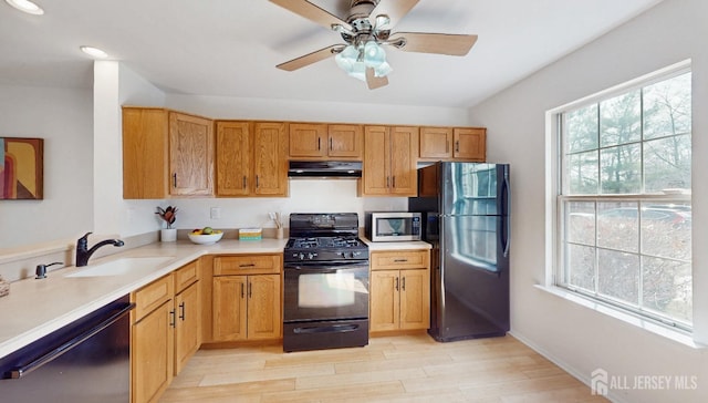 kitchen with light wood-style flooring, under cabinet range hood, a sink, light countertops, and black appliances