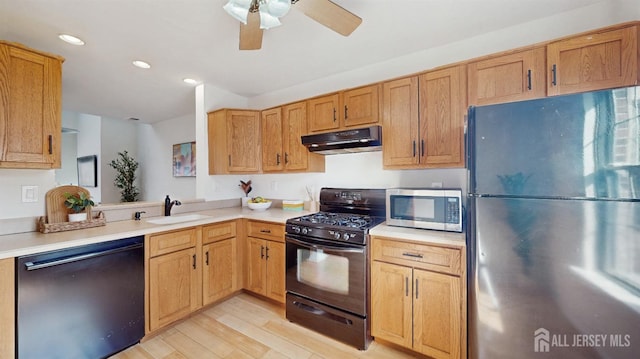 kitchen with light wood finished floors, under cabinet range hood, light countertops, black appliances, and a sink