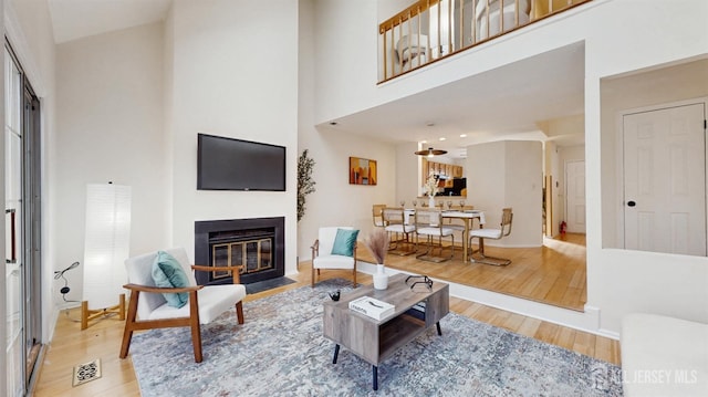 living room featuring visible vents, a towering ceiling, a fireplace with flush hearth, wood finished floors, and baseboards