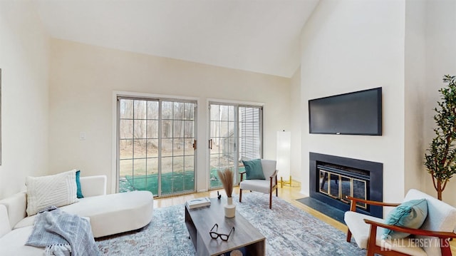 living room featuring high vaulted ceiling, wood finished floors, and a fireplace with flush hearth