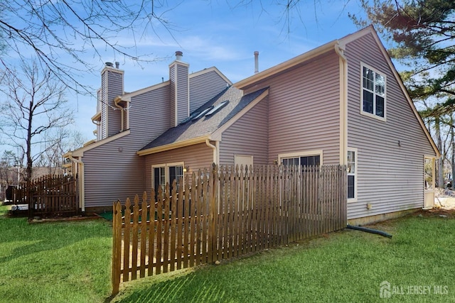 rear view of property with a chimney, fence, a lawn, and roof with shingles