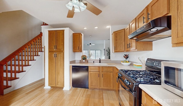 kitchen featuring light countertops, a sink, light wood-type flooring, under cabinet range hood, and black appliances