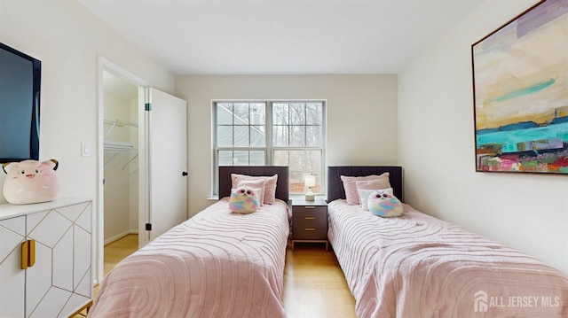 bedroom with a walk in closet and wood finished floors