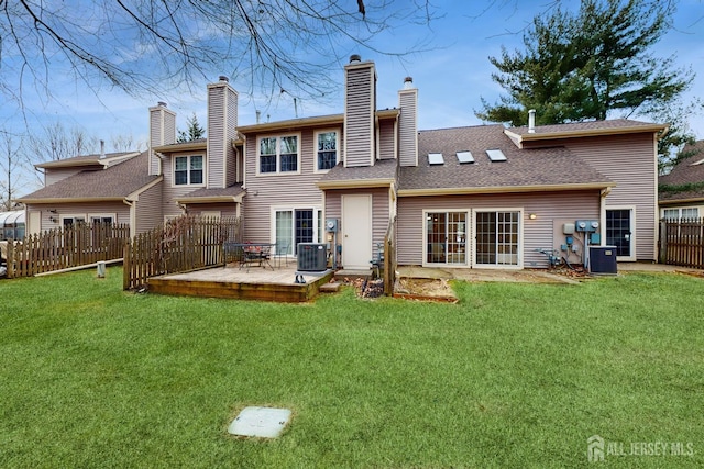 rear view of house with a shingled roof, central AC, fence, and a lawn