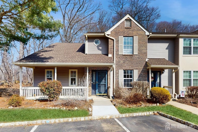 view of front of property with a porch, roof with shingles, brick siding, and uncovered parking