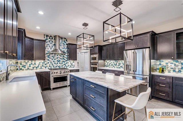 kitchen with sink, high end appliances, a center island, hanging light fixtures, and wall chimney range hood