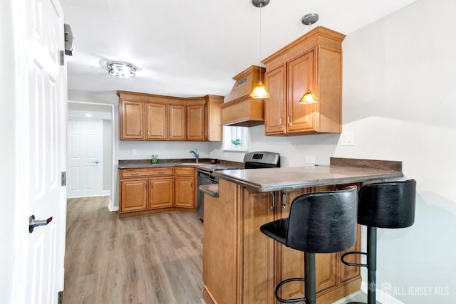 kitchen featuring dark countertops, light wood finished floors, brown cabinets, a kitchen breakfast bar, and hanging light fixtures