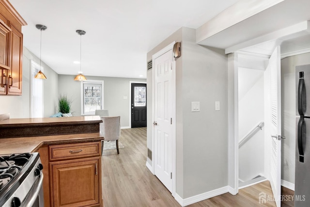 kitchen featuring light wood finished floors, brown cabinets, pendant lighting, and dark countertops