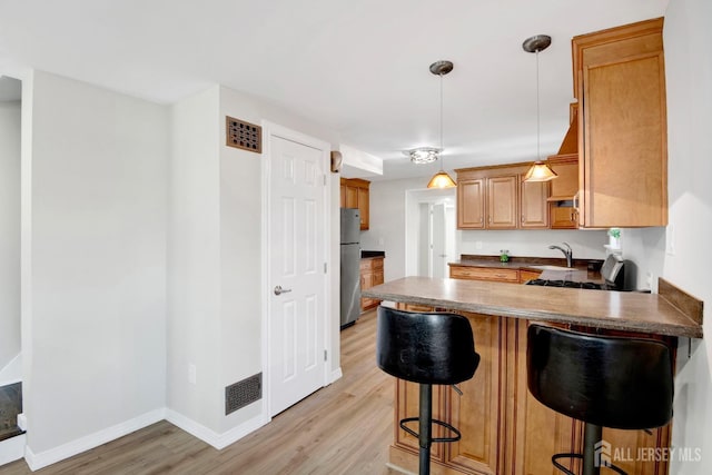 kitchen with a breakfast bar area, a peninsula, light wood-style flooring, freestanding refrigerator, and a sink