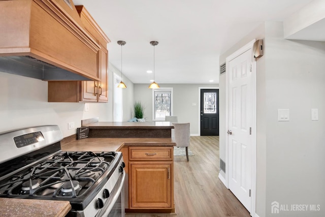 kitchen with dark countertops, premium range hood, a peninsula, light wood-style flooring, and gas range