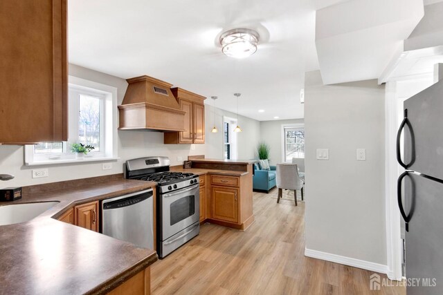 kitchen featuring dark countertops, stainless steel appliances, a peninsula, custom exhaust hood, and a healthy amount of sunlight