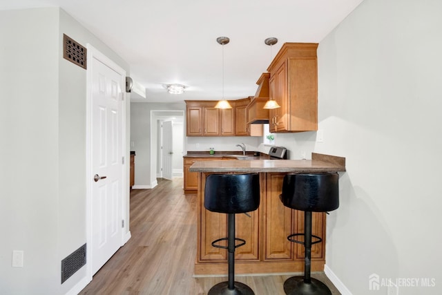 kitchen featuring a kitchen bar, a sink, light wood-style floors, a peninsula, and stove