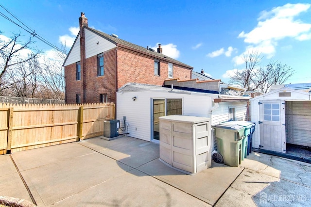 back of property featuring cooling unit, a storage shed, brick siding, a chimney, and a patio area