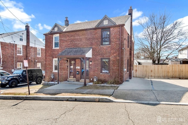 view of front of house with brick siding, a chimney, and fence