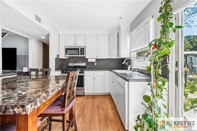 kitchen featuring stainless steel appliances, a sink, dark countertops, light wood finished floors, and white cabinetry