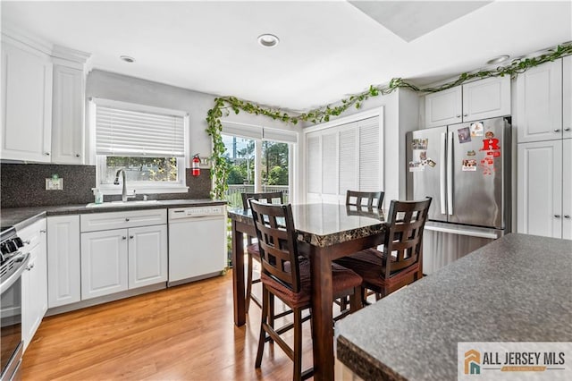 kitchen featuring dishwasher, freestanding refrigerator, a sink, dark countertops, and white cabinetry