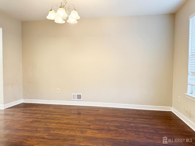 spare room with baseboards, a healthy amount of sunlight, dark wood-style floors, and an inviting chandelier