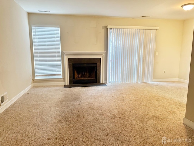 unfurnished living room featuring visible vents, baseboards, a fireplace with flush hearth, and carpet floors