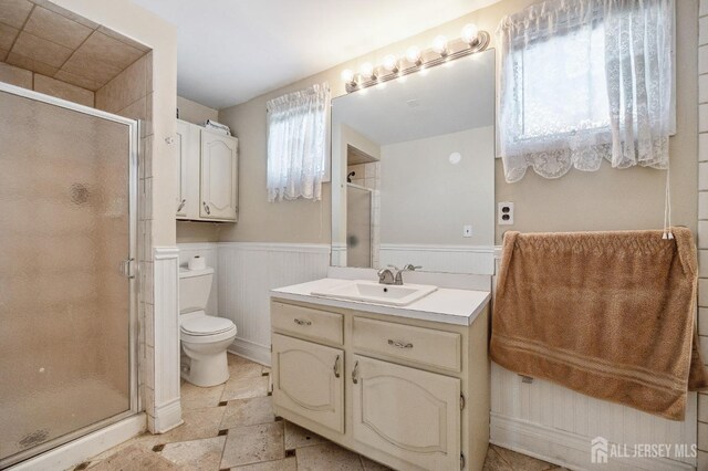 full bathroom featuring toilet, a wainscoted wall, vanity, and a stall shower