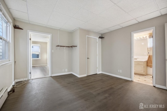 unfurnished bedroom with dark wood-style floors, multiple windows, baseboard heating, and a paneled ceiling