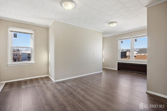 spare room featuring crown molding, dark wood-type flooring, baseboards, and radiator