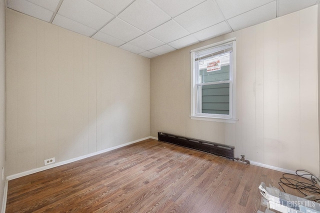 spare room with a drop ceiling, wood finished floors, a baseboard radiator, and baseboards