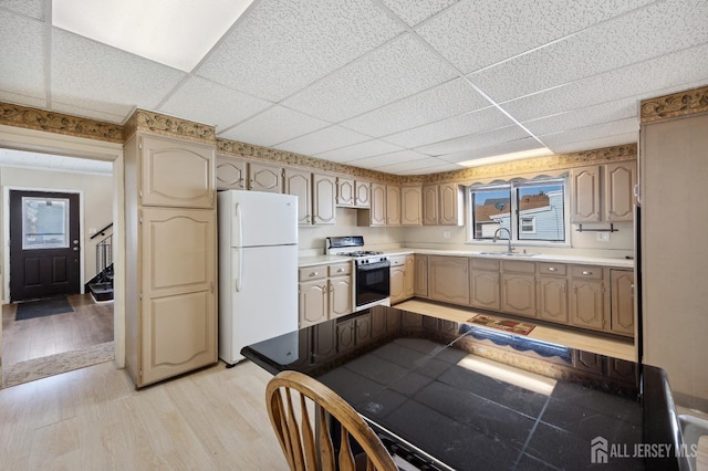 kitchen with a paneled ceiling, light countertops, light wood-style floors, a sink, and white appliances