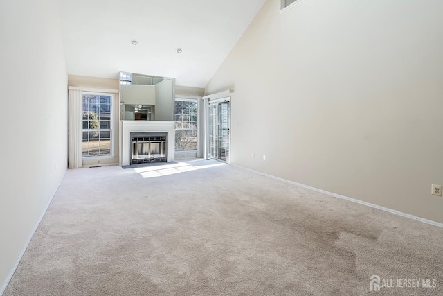 unfurnished living room with baseboards, light carpet, high vaulted ceiling, and a fireplace with flush hearth