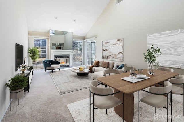 dining room featuring light carpet, a glass covered fireplace, a healthy amount of sunlight, and high vaulted ceiling