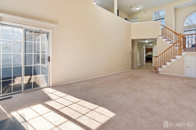 unfurnished living room featuring stairs, a high ceiling, visible vents, and carpet