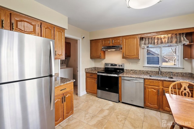 kitchen with a sink, washer / dryer, brown cabinets, under cabinet range hood, and appliances with stainless steel finishes