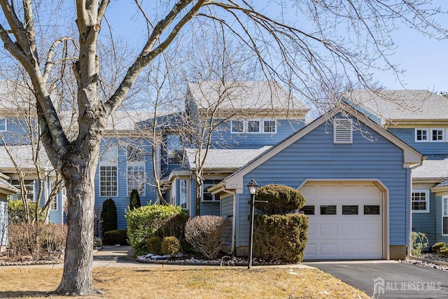 traditional-style house featuring an attached garage, a shingled roof, and driveway