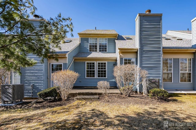 back of property featuring a chimney, central air condition unit, and a shingled roof