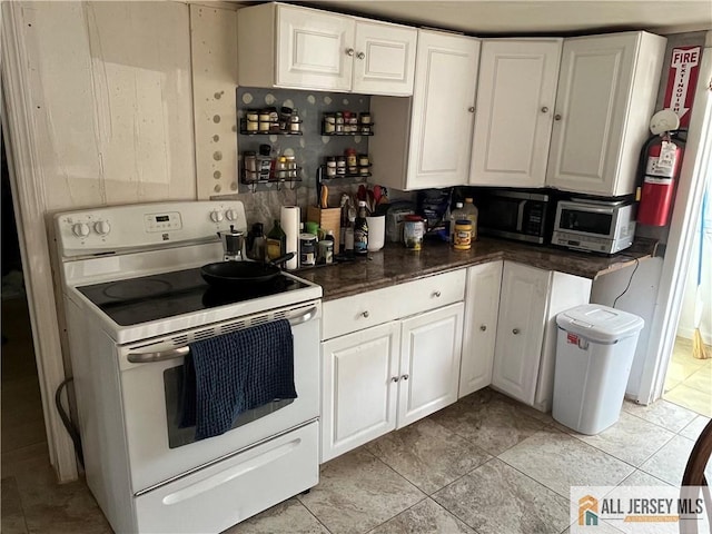 kitchen with white electric range, dark countertops, light tile patterned flooring, and white cabinetry