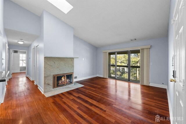 unfurnished living room featuring lofted ceiling with skylight, wood-type flooring, a wealth of natural light, and a high end fireplace