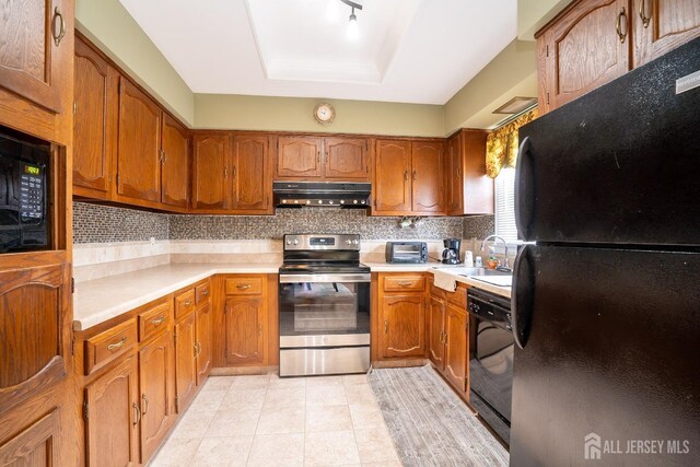 kitchen with tasteful backsplash, black appliances, sink, light tile patterned floors, and a tray ceiling