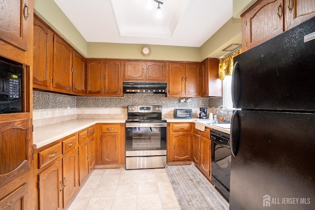 kitchen featuring under cabinet range hood, a tray ceiling, light countertops, black appliances, and a sink