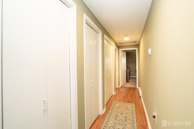 corridor featuring a textured ceiling and light hardwood / wood-style flooring