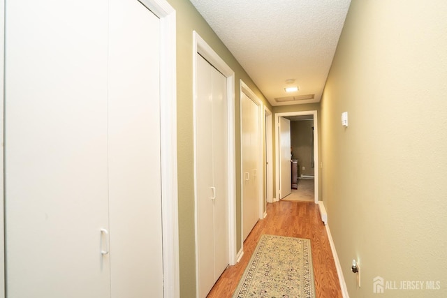 hall with a textured ceiling, light wood-style flooring, and baseboards