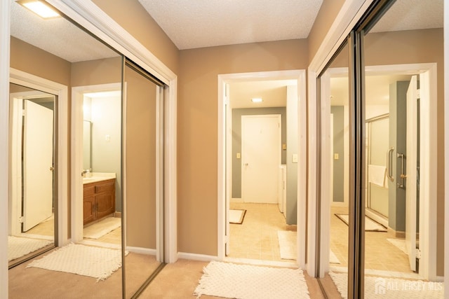 hall with light colored carpet, a textured ceiling, and baseboards