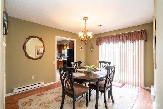 dining area with light wood-type flooring, a textured ceiling, a notable chandelier, and baseboard heating