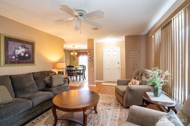 living room featuring ceiling fan with notable chandelier, a textured ceiling, and light wood-type flooring