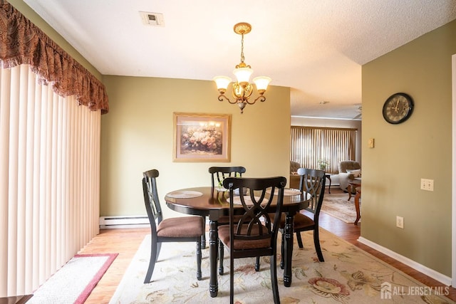 dining space with a baseboard heating unit, a textured ceiling, a notable chandelier, and light hardwood / wood-style floors