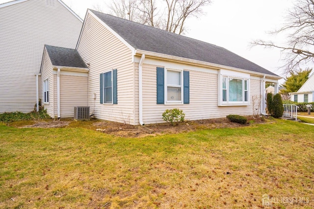 view of side of property with a yard, a shingled roof, and central AC