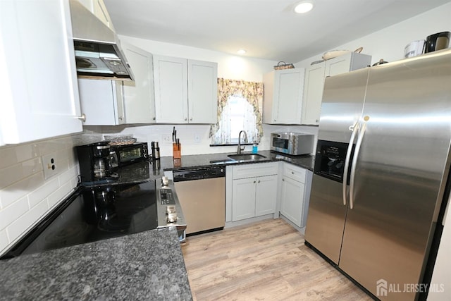 kitchen featuring appliances with stainless steel finishes, a sink, ventilation hood, decorative backsplash, and dark stone countertops