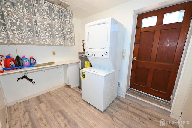 laundry area featuring stacked washer / drying machine, water heater, and light wood finished floors