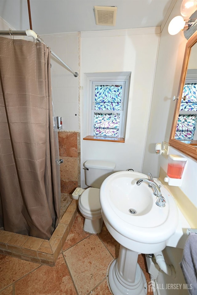 full bath featuring a shower stall, stone tile floors, and toilet