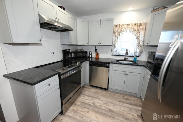 kitchen with appliances with stainless steel finishes, under cabinet range hood, a sink, tasteful backsplash, and dark stone counters